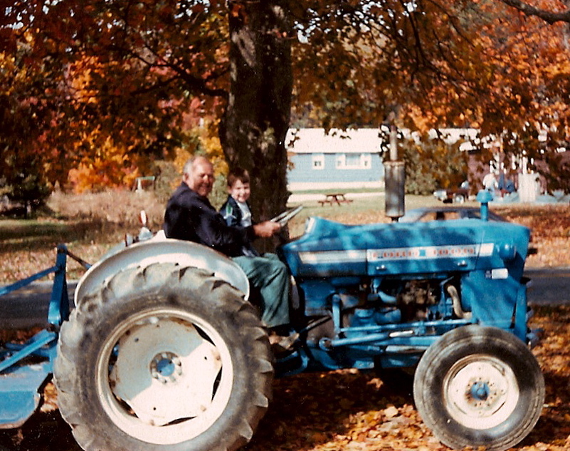 Melvin Estabrook and a child riding a blue Ford tractor